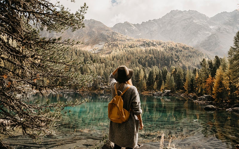 Donna con zaino e cappello ammira un lago nella foresta