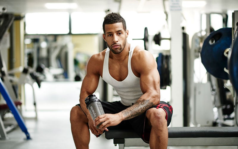 homme assis sur un banc de muscu, les fibres musculaires de ses biceps sont légèrement contractées