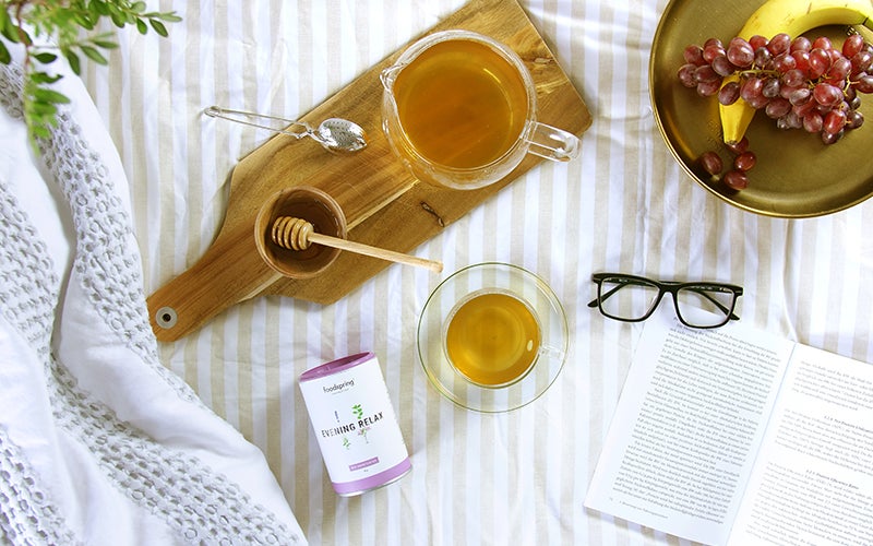 A canister of Evening Relax tea sits next to a glass mug and a honey bowl with a dipper. A warm tea can help when it's too hot to sleep