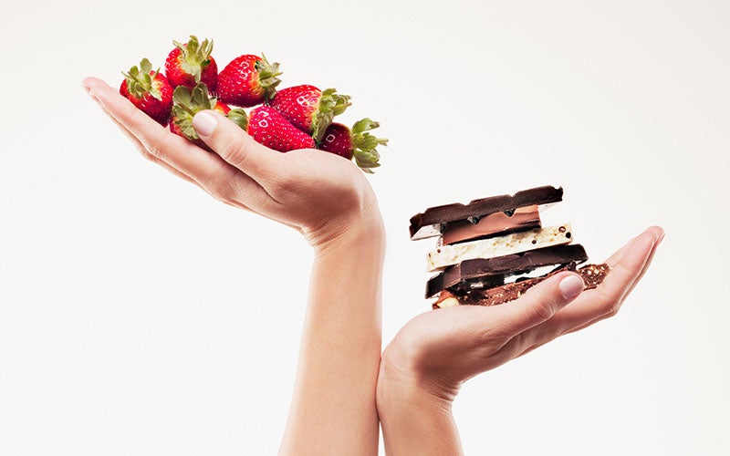 A pair of white hands cup food in their palms. The left hand holds fresh strawberries, while the right cradles a stack of chocolate bars.