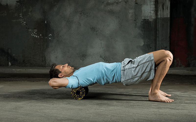 A white man in fitness clothing performs foam roller exercises by rolling his upper back over a foam roller