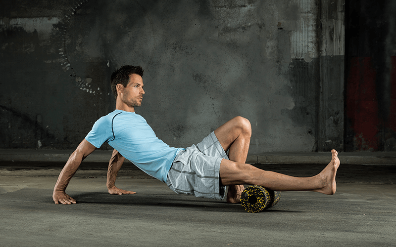 A white man in fitness clothing performs foam roller exercises by rolling his calf over a foam roller