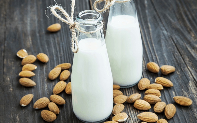 Two glass bottles filled with vegan milk and surrounded by almonds