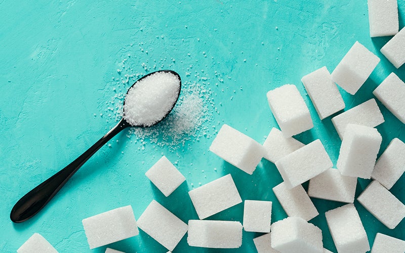 A dozen sugar cubes on a light blue-green background with a black spoon filled with granulated sugar