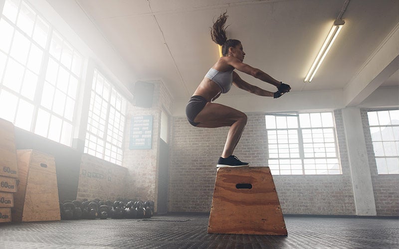 A white woman with long brown ponytail swinging above her head practices box jumps in hopes of achieving the afterburn effect