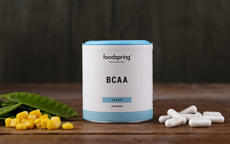 A package of BCAA capsules with corn kernels, snap peas, and capsules surrounding it 