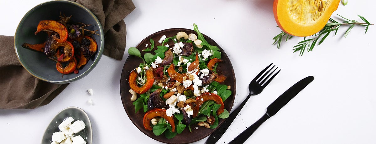 A photo from above of a pumpkin salad topped with crumbled white cheese, nuts, and berries