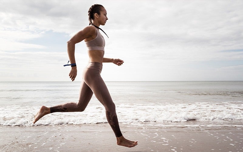 how to lose weight without dieting? the simplest is exercise, as shown by this medium-skin-toned woman running on the beach with waves breaking near her bare feet.
