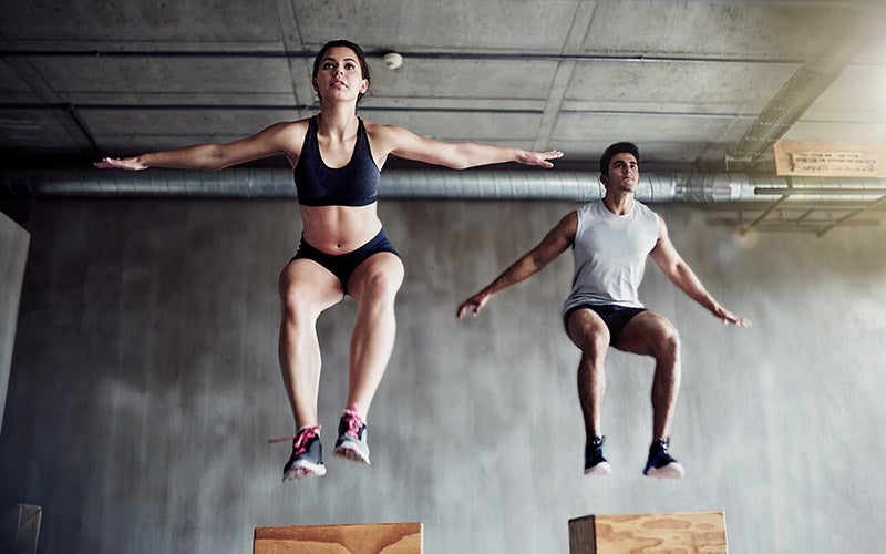 Photo of a white-presenting woman and man jumping onto crates during fascia training