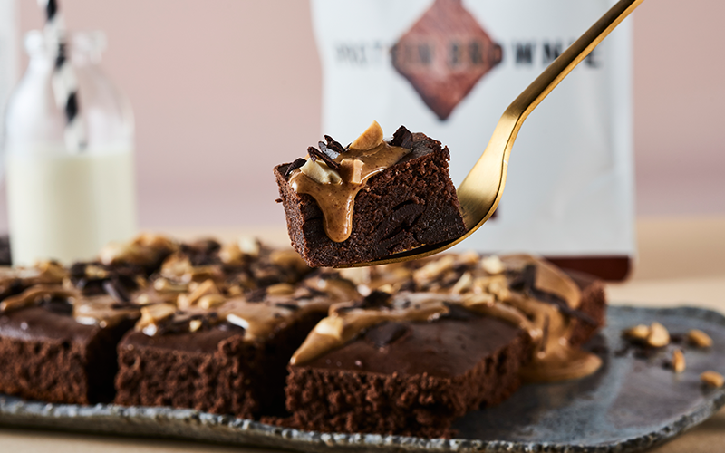 A gold fork holds a bite of foodspring protein brownie