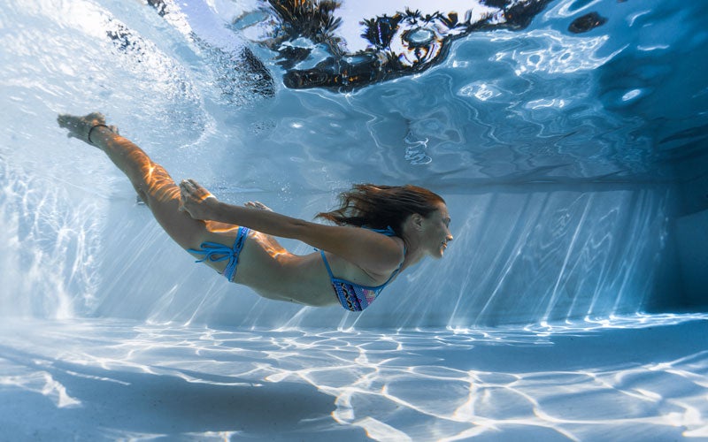 a white woman in a two-piece swimsuit dives under the water showing the benefits of swimming