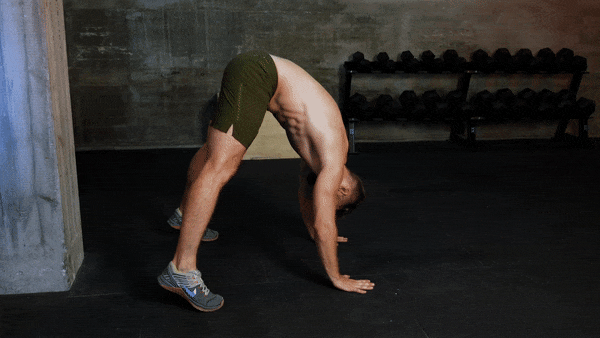 A shirtless white athlete goes from the peak push-up position to rolling his body forwards in a somersault, as he learns how to do a handstand.