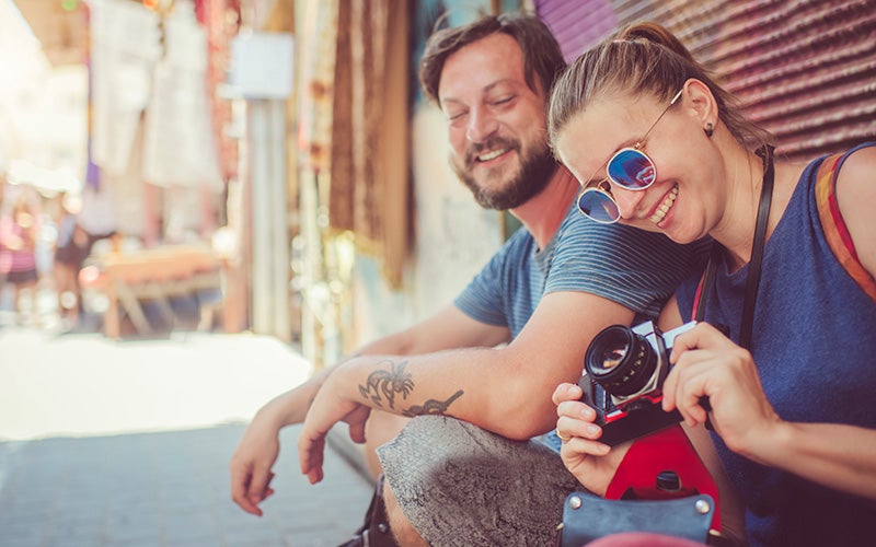 Giovane coppia di turisti seduta sul marciapiede fa una foto con una macchina fotografica