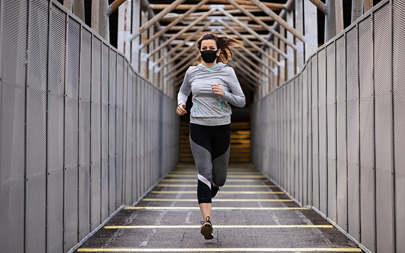 Frau joggt mt Maske über eine Brücke