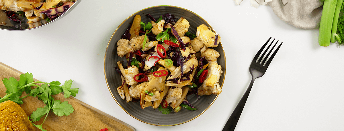 A dark gray bowl full of spiced cauliflower florets, topped with red onion and pepper slices