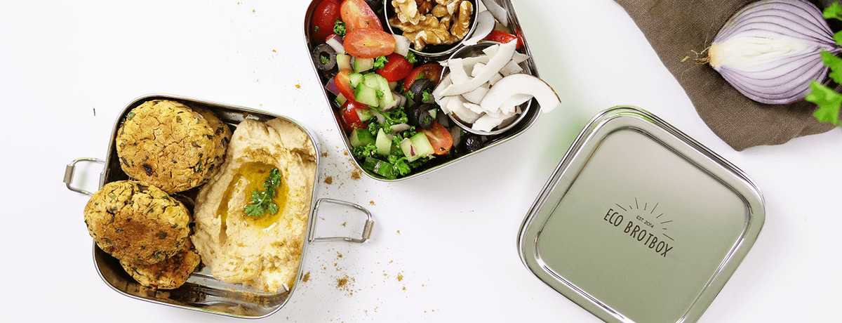 A stainless steel lunch box packed with hummus, falafel, and a tomato-cucumber salad