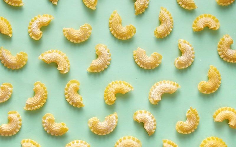 Evenly-spaced, uncooked creste di galli (cockscomb) pasta on a sea-green background