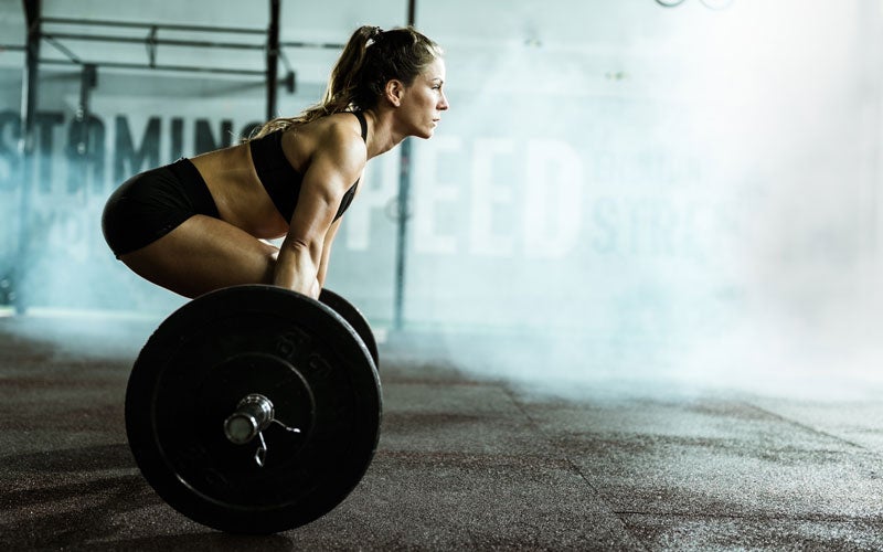 A white woman prepares herself to deadlift a barbell with large weight plates in a gym.