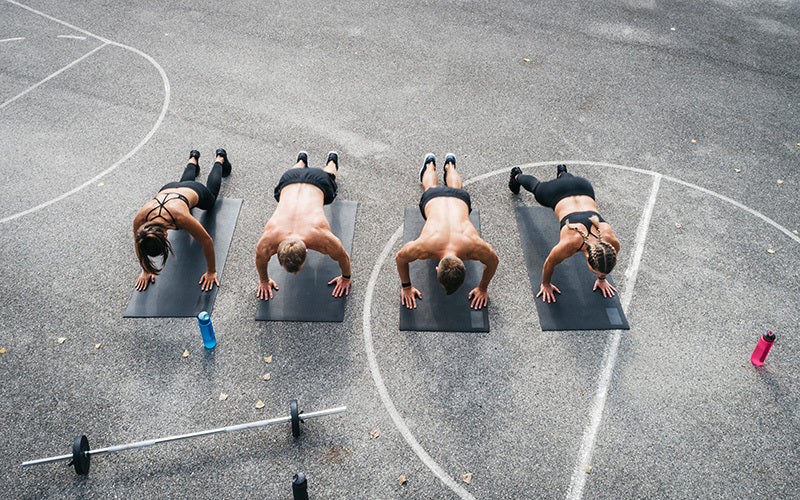 A group of two white men and two white women do push-ups together on a basketball court