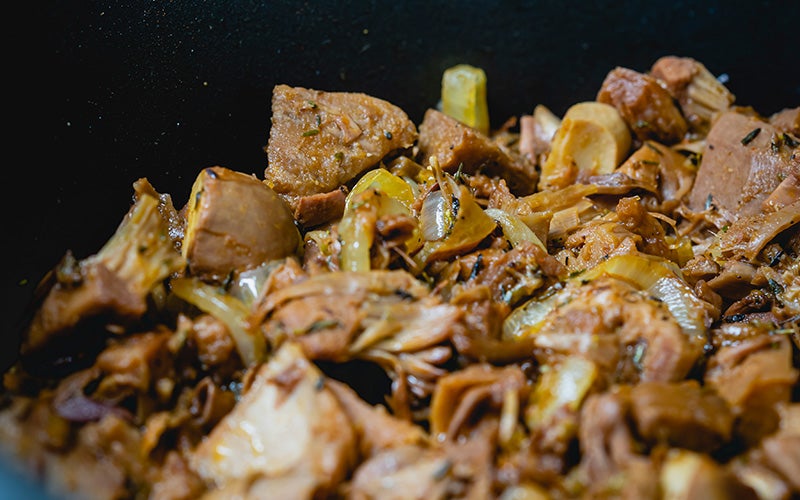 a close-up view of a pan of jackfruit and onions in a pan with unknown spices. The jackfruit is browned and the onions have a clear-golden hue.