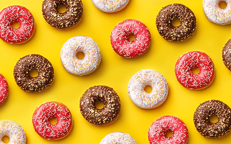 A photo of chocolate-brown, dark-pink and white-glazed donuts in a pattern on a vibrant yellow background