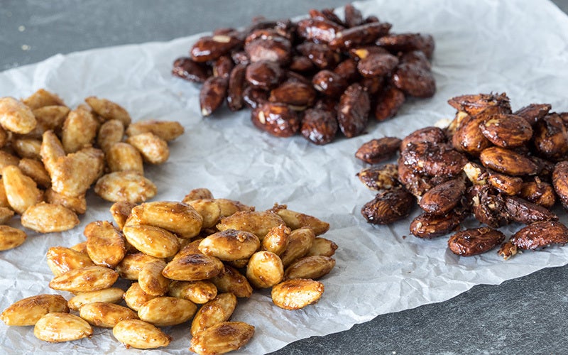 A photo of four varieties of candied almonds ranging in color from dark brown to light tan on white parchment paper