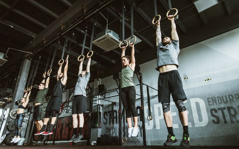 A group of men and women hang from wooden rings at a gym