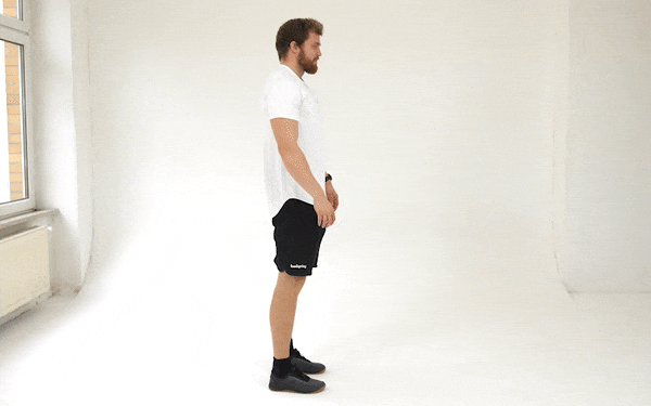 A GIF of a white man in a white t-shirt and black shorts bending down to touch his toes. His legs do not bend. He moves his pelvis backwards as he bends down, allowing his knees and back to stay straight and hinge only at his waist. He easily touches his fingertips to the ground and rests his palms on the toes of his shoes.