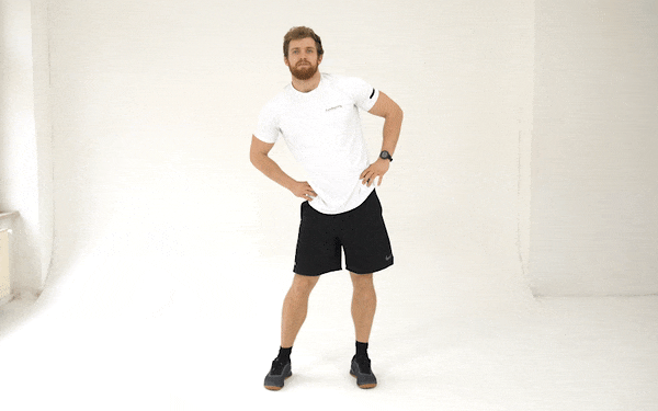 A GIF of a white man in a white t-shirt and black shorts doing hip circles. He stands with his feet shoulder-width apart and hands on hips. He moves his hips in a circle to his left, then after a full circle, he switches and circles them to the right.