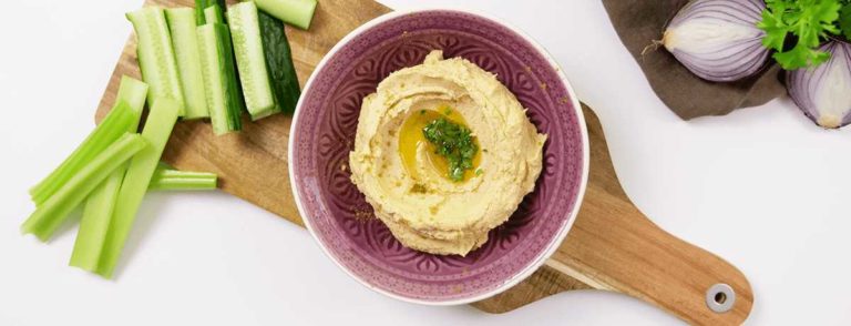 A photo of a bowl of hummus with some celery and cucumber sticks next to it