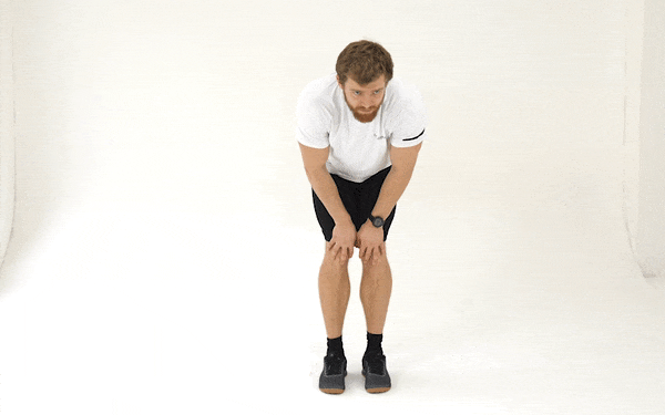 A GIF of a white man in a white t-shirt and black shorts doing knee circles. He bends down, keeping his back straight, and resting his hands on his knees. He moves each knee outwards and straightens them a bit as he circles, then returns to the starting position and circles them inwards.