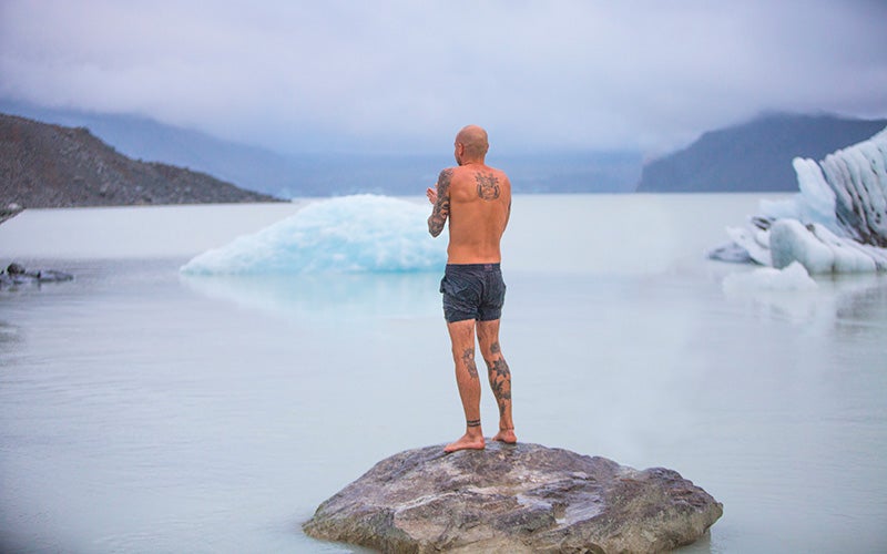 Mann steht auf einem Fels vor einem fast zugefrorenem See