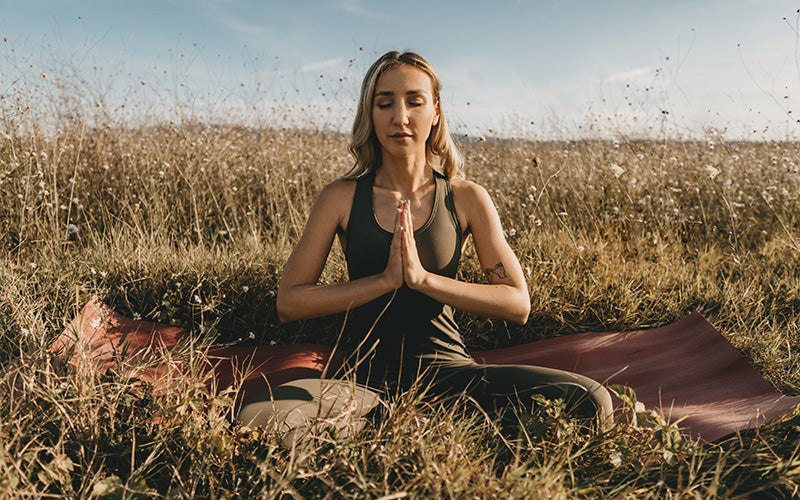 Frau sitzt in einer Yoga Pose auf einer Wiese und macht Atmenübungen