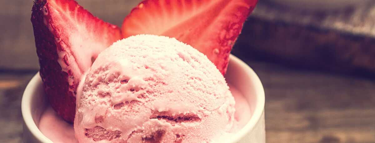A scoop of Protein Low Carb strawberry ice cream with a halved strawberry framing the scoop on each side