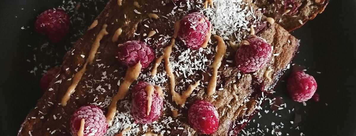 A chocolatey energy protein cake drizzled with chocolate and topped with powdered sugar and fresh raspberries