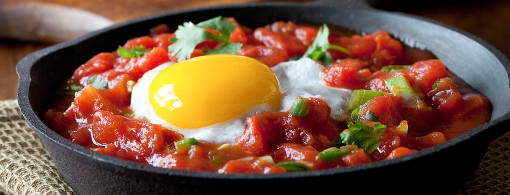 A photo of a soft-cooked, sunny-side-up egg over a tomatoey sauce.