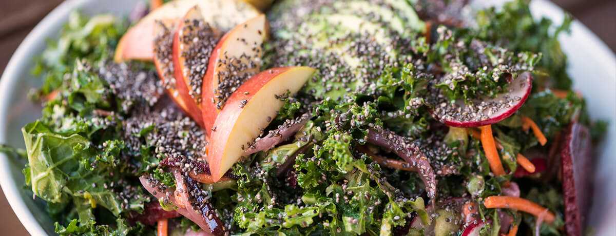 a close zoom of a bowl of curly kale salad topped with thinly sliced apples and chia seeds