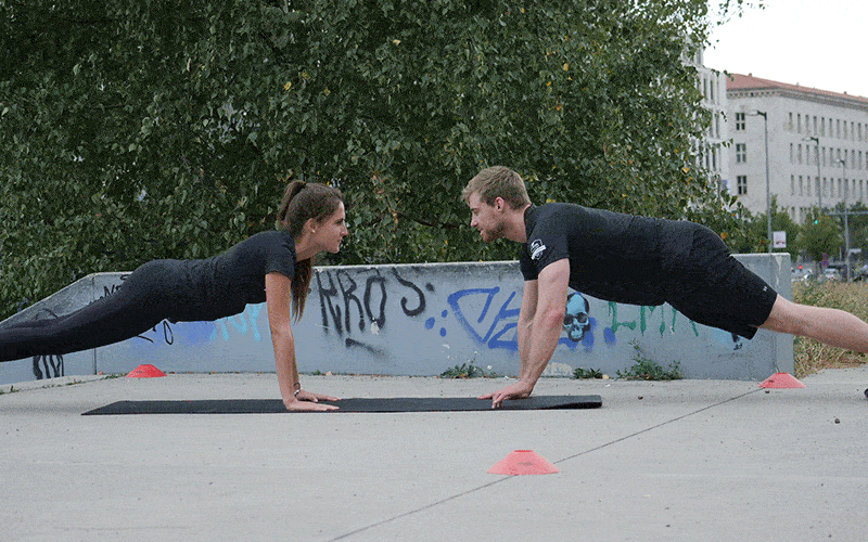 GIF image of a white man and a white woman doing partner clap pushups outdoors