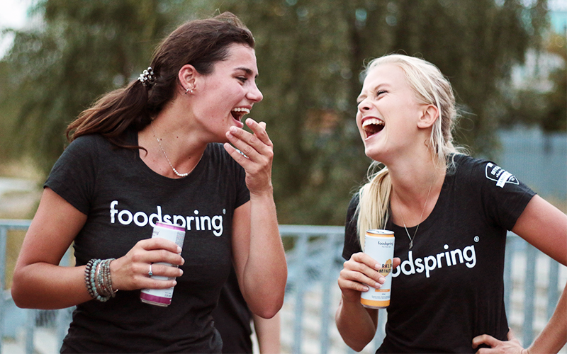 Two laughing white women in foodspring t-shirts after partner workouts