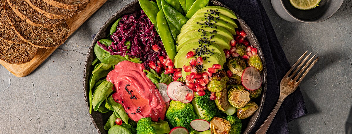A color-packed winter Buddha bowl with avocado slices, pomegranate seeds, beetroot hummus, Brussels sprouts, and more