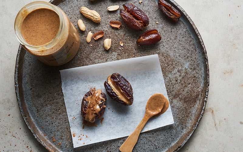 Two peanut-butter-filled date snacks sit on a piece of parchment paper, laid on a gray-brown plate.