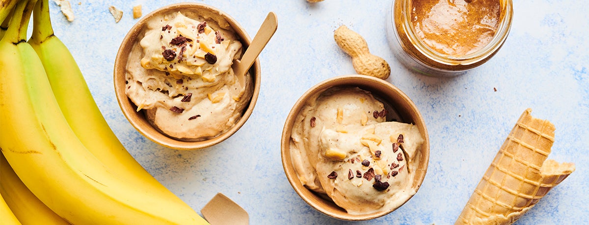 a photo of bananas next to two containers of banana-peanut butter nice cream