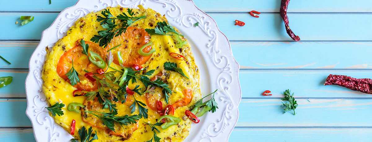 A photo of a feta and tomato omelet with lots of green herbs on a white plate