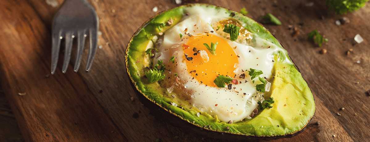 A photo of an egg cooked inside of an avocado, topped with salt, pepper and green herbs