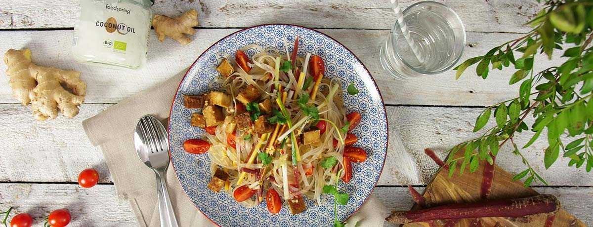 A photo from above of glass noodle salad with tofu, garnished with bright red accents, and with a spoon next to the plate