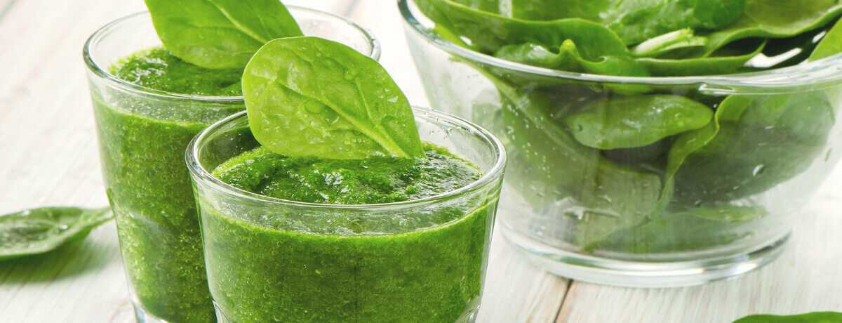 A glass of green smoothie garnished with a spinach leaf