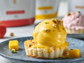 A scoop of gently melting mango protein ice cream and a scoop of strawberry protein ice cream in golden-brown edible ice cream cups