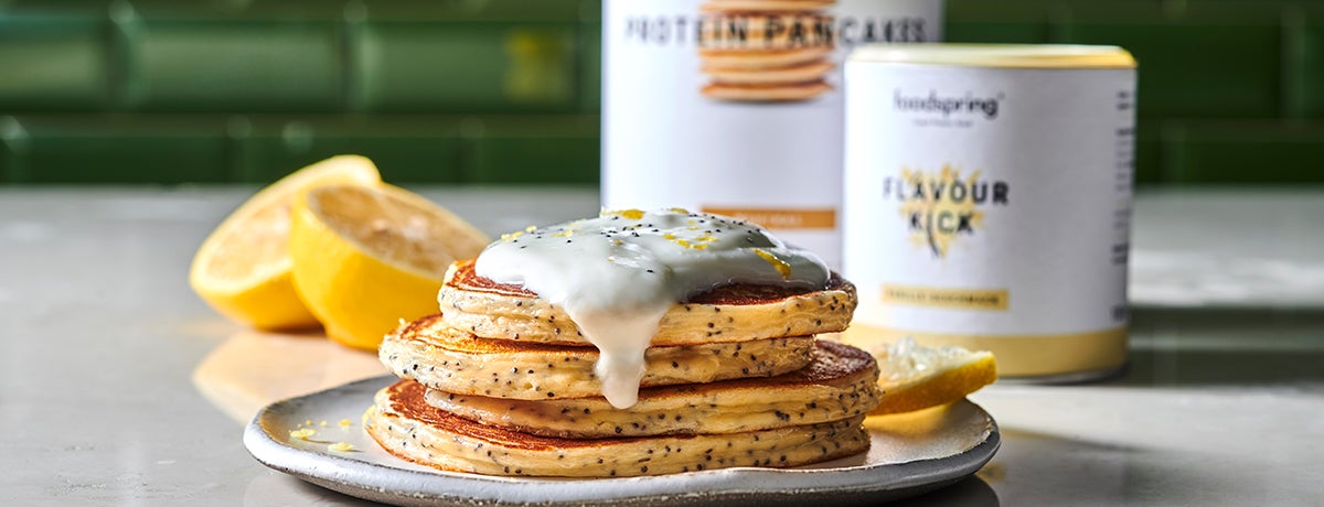 a photo of a stack of enticing lemon-poppyseed protein pancakes drizzled with cream and with lemon quarters in the background