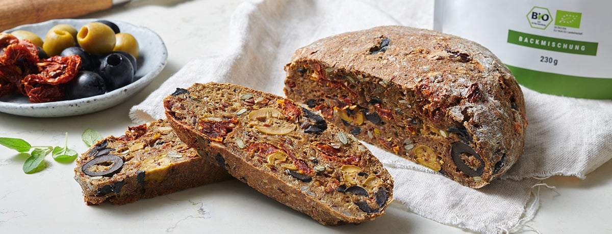 A photo of olive bread with sun-dried tomatoes, half a loaf sitting whole next to two slices.