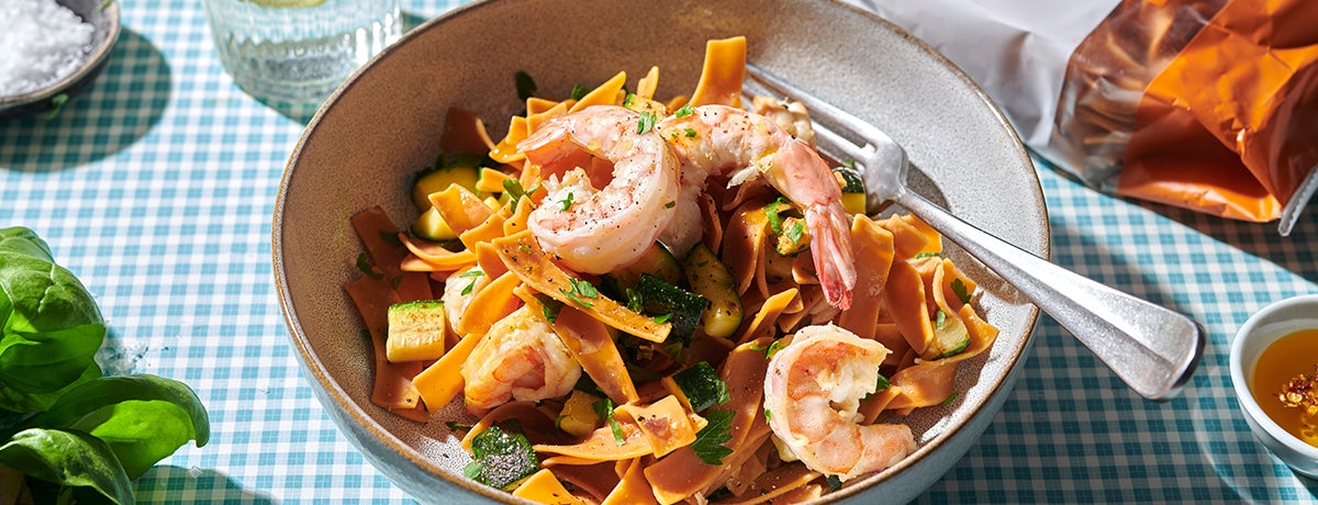 A bowl of orange-tinted Protein Pasta noodles with shrimp